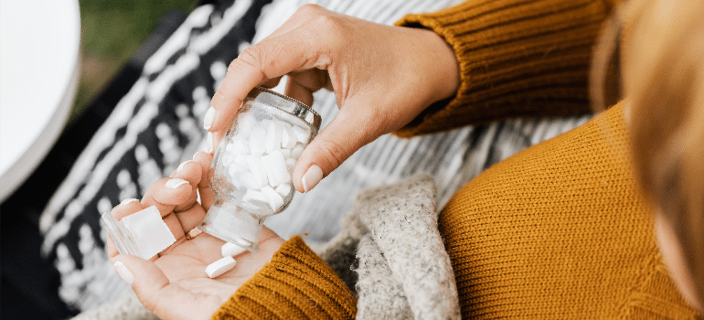 A close-up of a woman taking medicine from a bottle