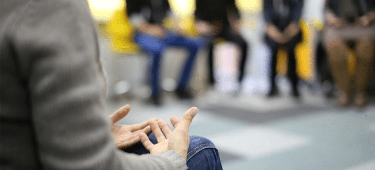 A close-up of a person opening up during a group therapy session and talking about Cognitive Behavioral Therapy in drug addiction treatment
