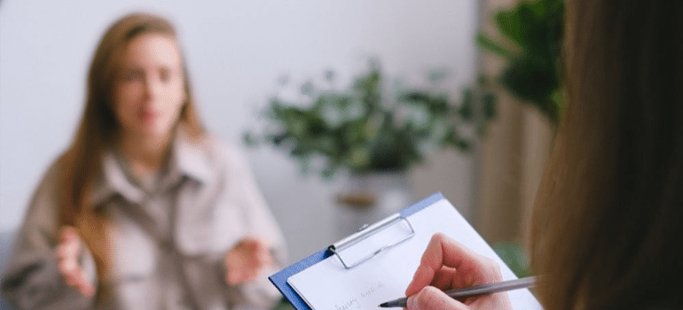 A woman in psychotherapy, as her therapist keeps notes.