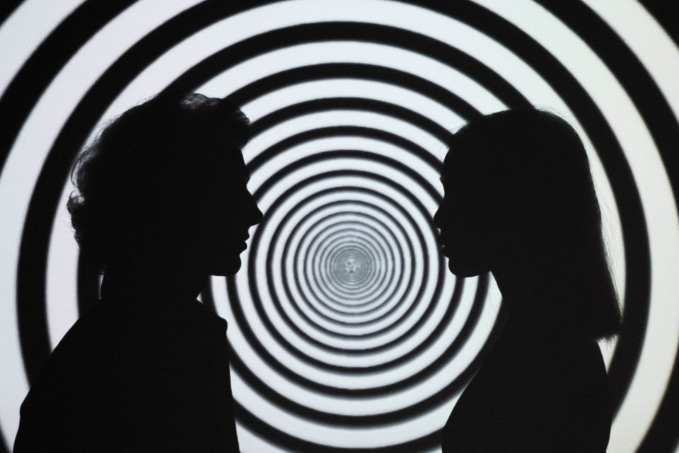 two silhouettes in front of a hypnotic pattern