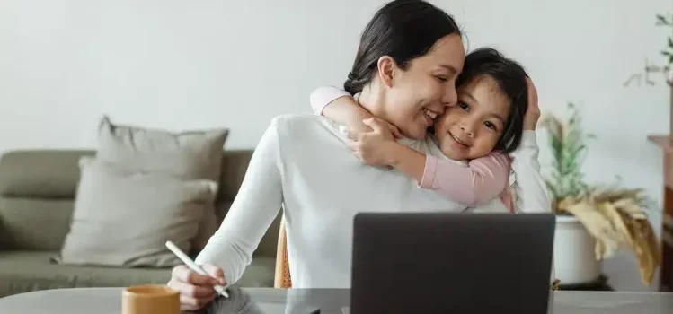 A mother working on the laptop and hugging her child