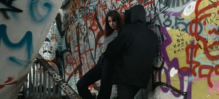 a woman and a man in black jacket standing beside graffiti wall talking about the risks of fentanyl laced heroin