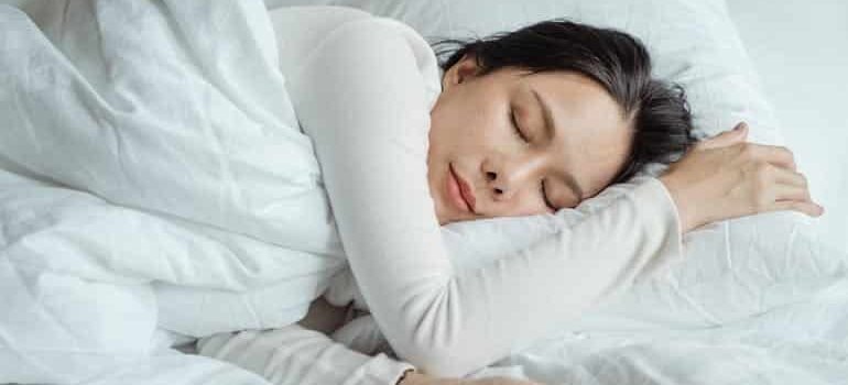 A woman sleeping in bed near her smartphone, showing efforts to rebuild healthy sleep habits after Adderall use.